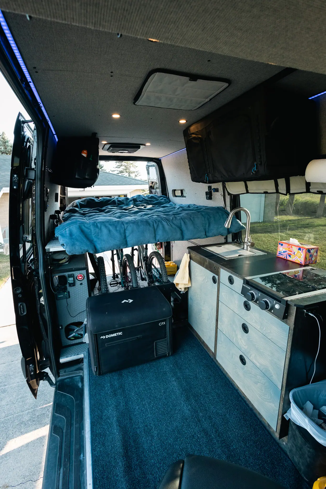 Sprinter camper van interior with a raised rear bed over mountain bike storage, a galley, stove and fridge