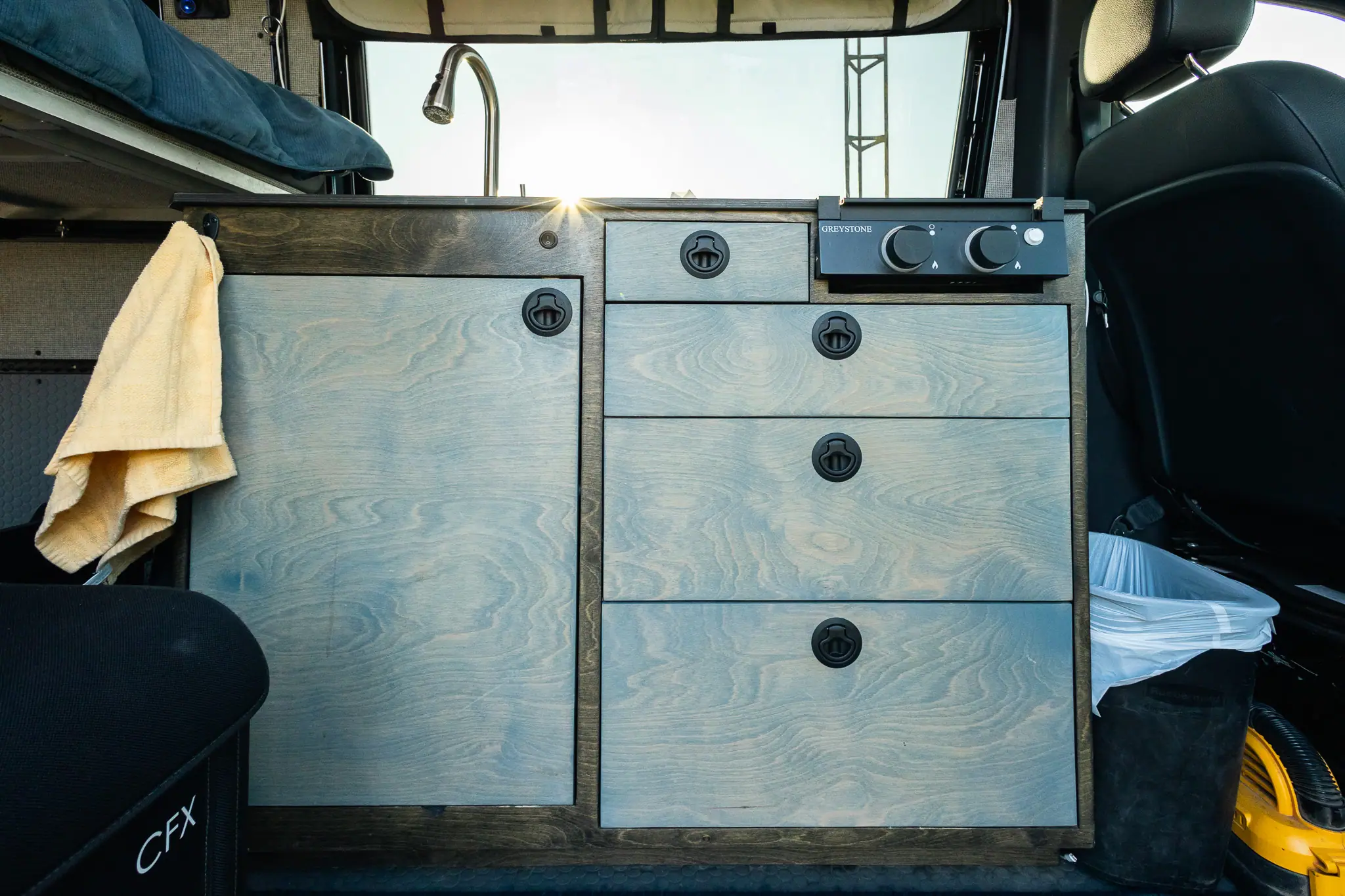 Custom blue-gray galley cabinet with drawers, black latches and a two-burner stove in a Sprinter camper van