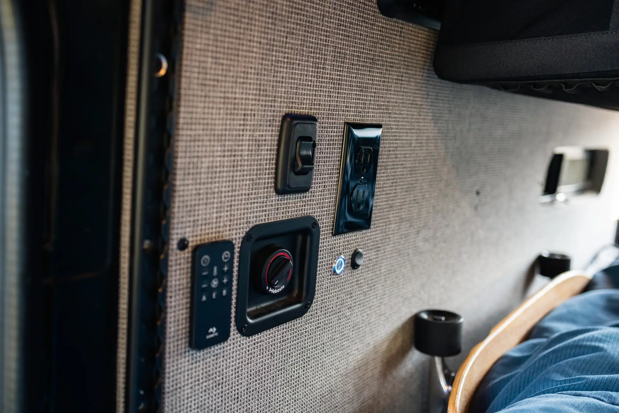 Heater control, 120V outlet and switches on a fabric-covered wall inside a Sprinter camper van