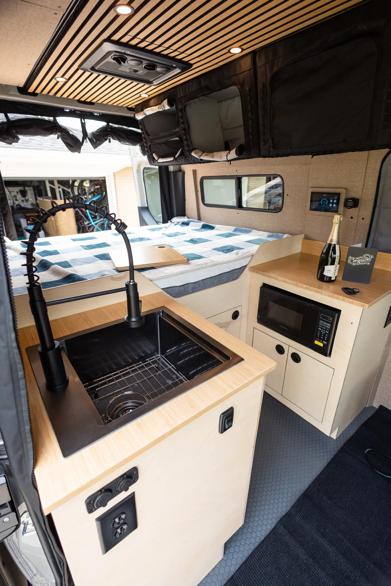 Sprinter camper van galley with a black sink, pull-down faucet, bamboo countertops and birch cabinets