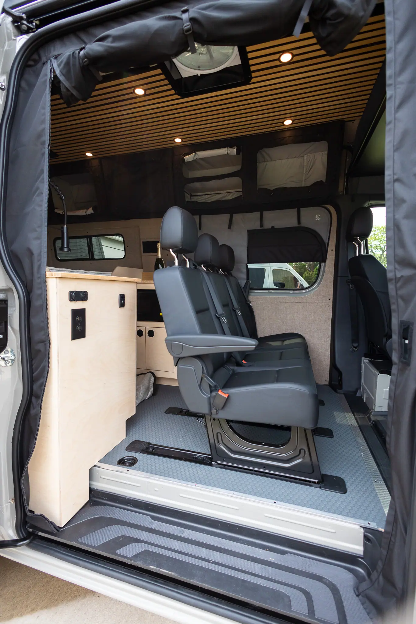 Three-passenger bench seat on floor rails inside a Sprinter camper van conversion