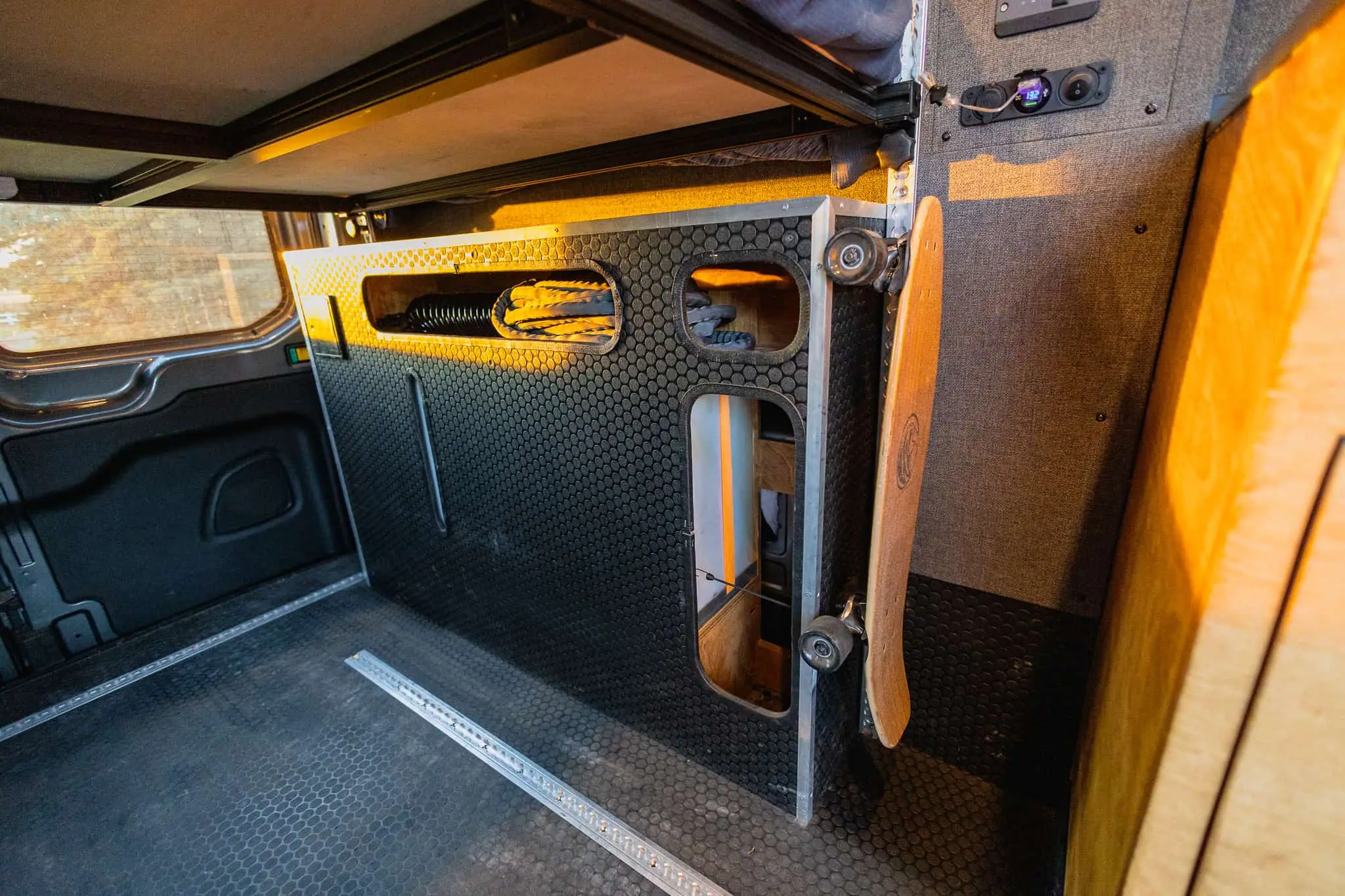 Under-bed gear storage boxes with cutout cubbies and a charging panel in a Ford Transit camper van