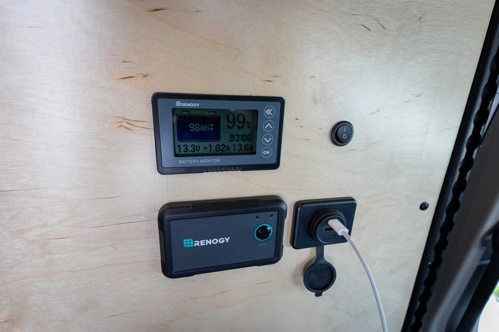 Battery monitor and USB charging ports mounted on the plywood wall of a Ford Transit van